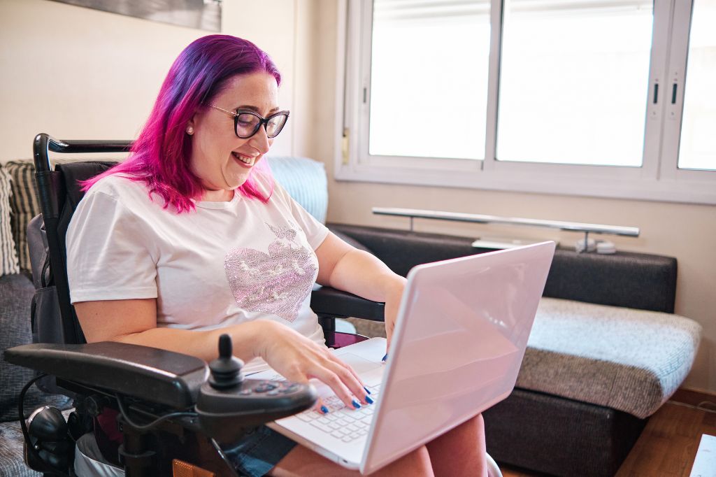 Woman with pink hair on her laptop while sat in a wheelchair